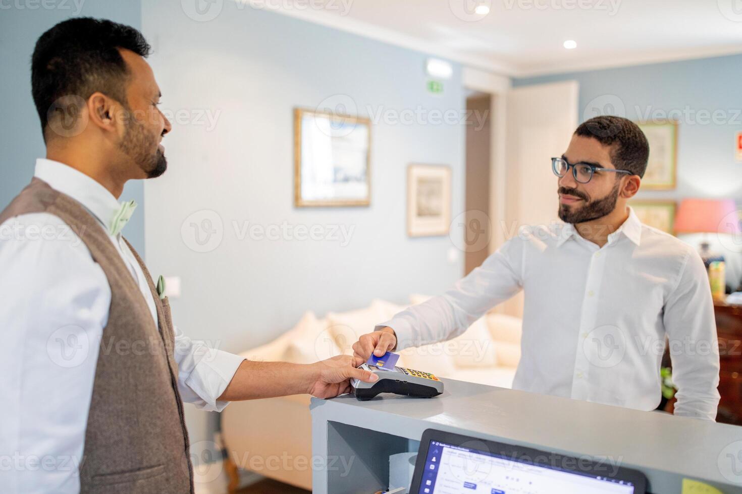 A customer in a white shirt is completing a payment at the hotel reception desk. The staff member helps facilitate the transaction, ensuring a smooth check-in experience. photo