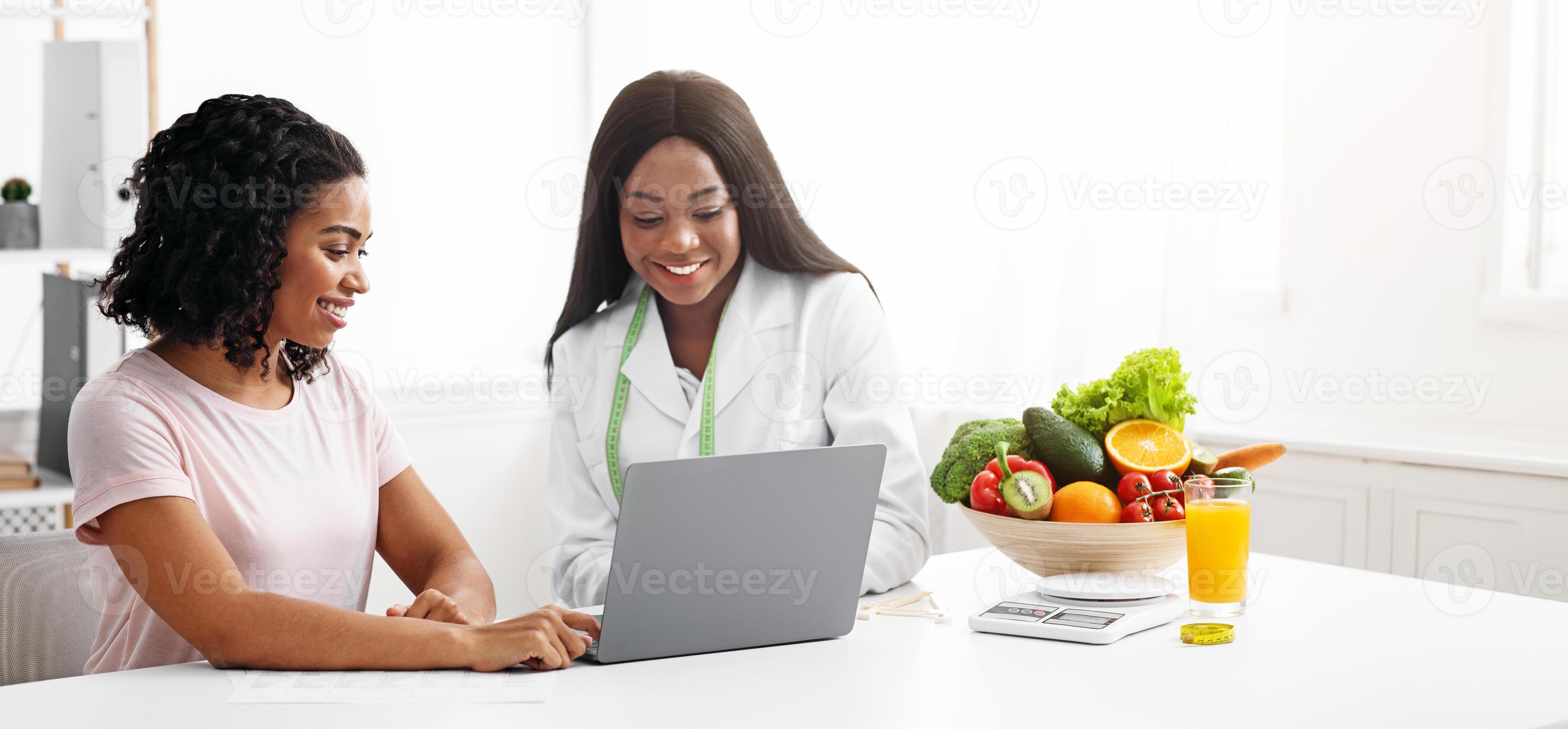 Black women nutritionist and patient looking at laptop screen at clinic Black women nutritionist and patient looking at laptop screen at clinic