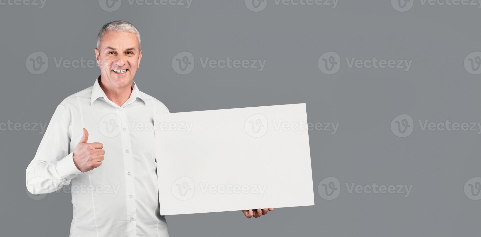 I Recommend. Smiling Senior Man Holding Blank Placard With Copy Space, Showing Thumbs Up, Gray Studio Wall photo