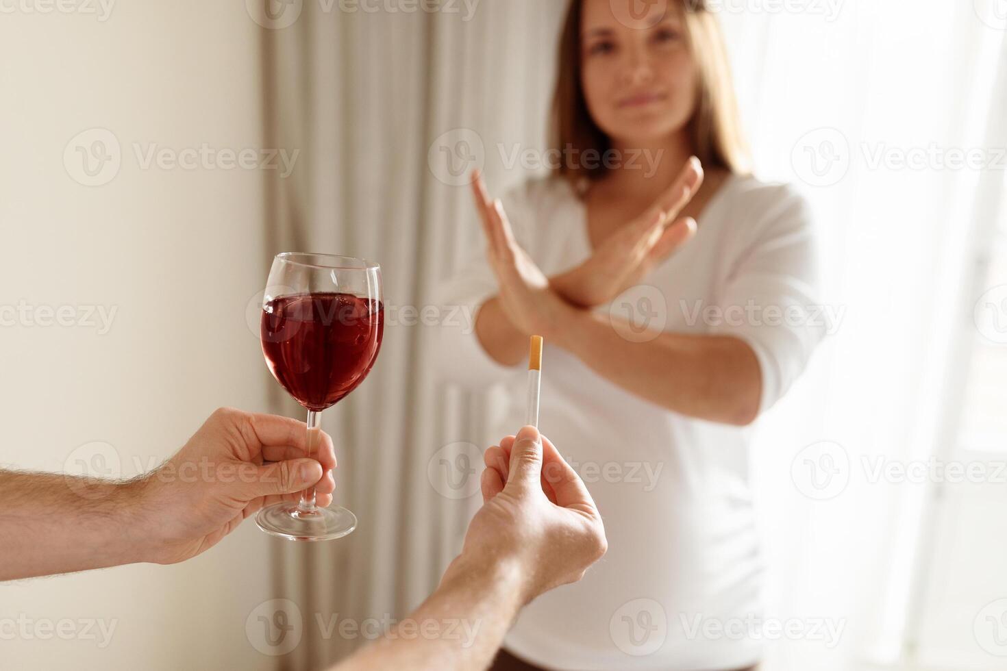 A woman with a serious expression is politely rejecting a glass of red wine offered to her. She holds a test stick in her other hand, indicating a significant decision. photo