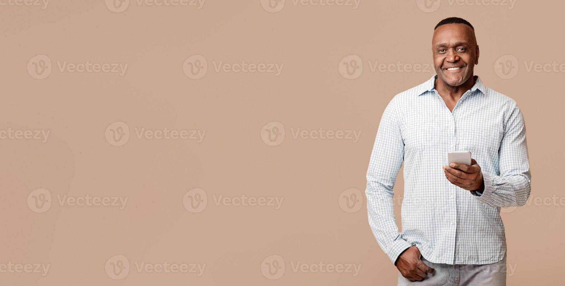 Always in touch. Handsome mature african man networking on cellphone, orange studio background photo