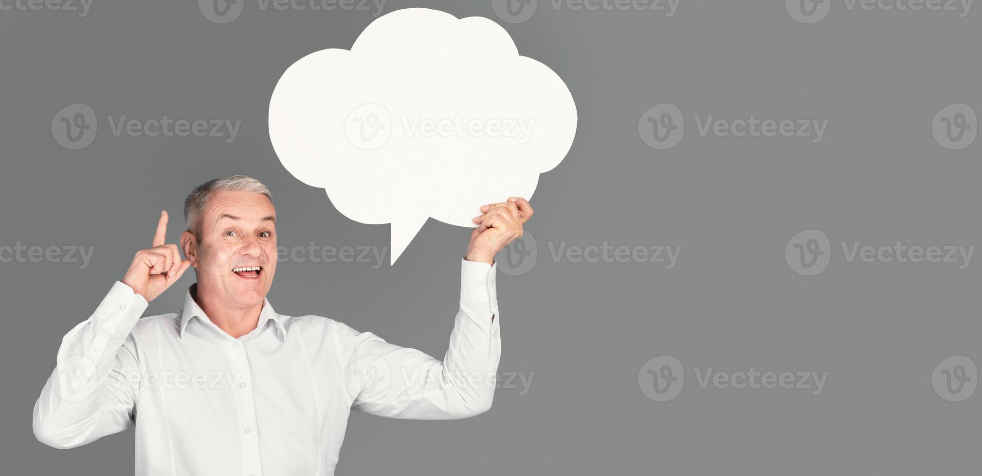 I Have An Idea. Glad senior man holding blank speech bubble, pointing finger up, copyspace, gray studio wall photo