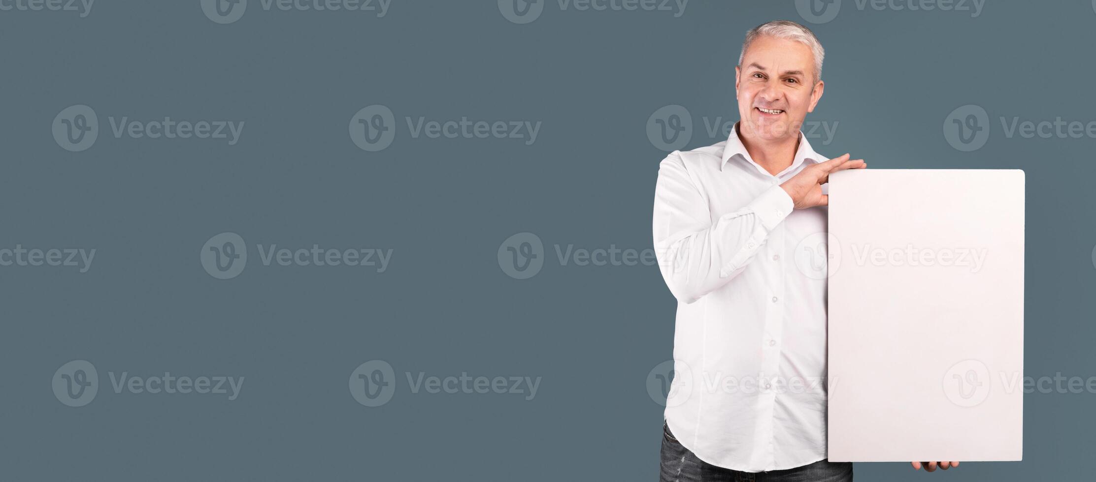 Happy Mature Man Showing Vertical Blank Placard With Copy Space For Your Text Isolated Over Blue Studio Wall photo