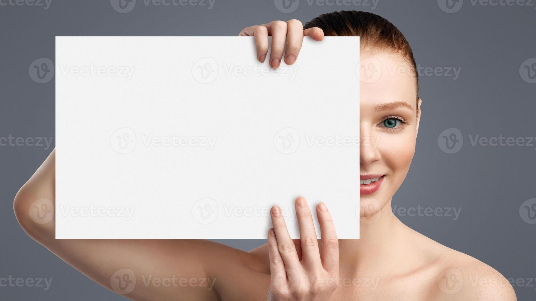 Makeup Concept. Young Female Holding White Paper Board Covering Half Of Face Looking At Camera Posing In Studio Over White Background. Headshot Of Pretty Woman With Poster For Text photo