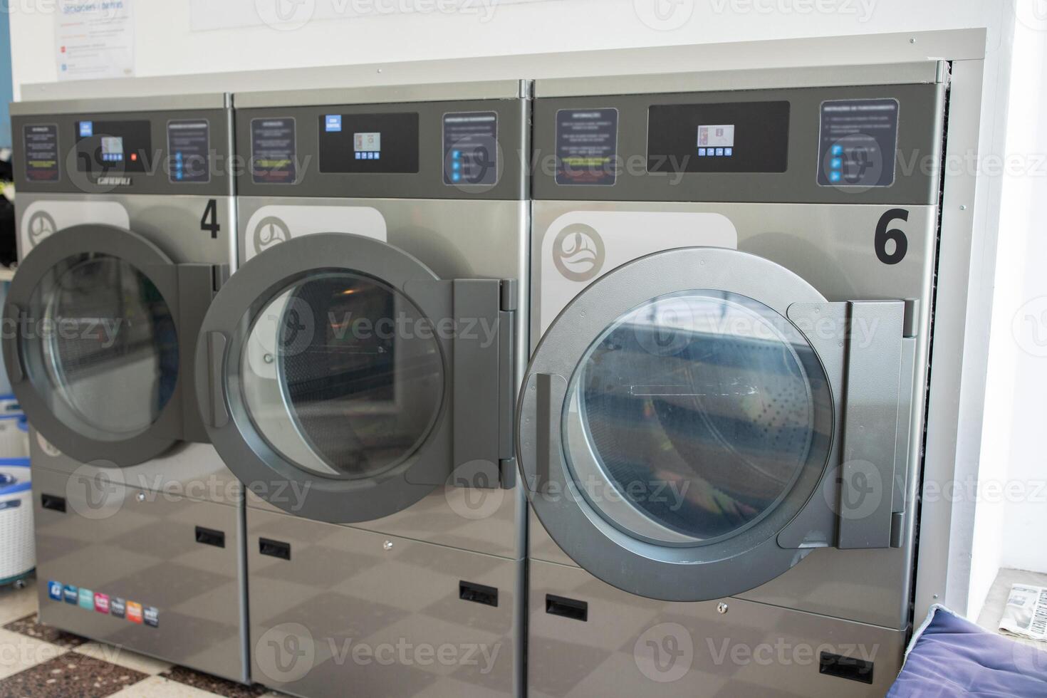 Three sleek coin-operated washing machines lined up in a tidy laundromat, featuring a bright interior with clear digital displays and spacious surroundings. photo