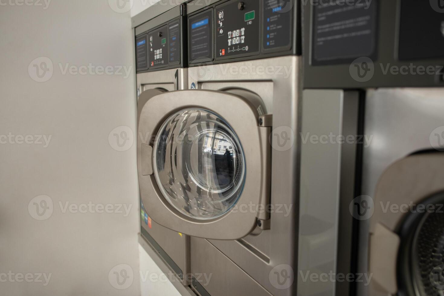 A row of sleek, stainless steel laundry machines is operational in a self-service laundromat during the late afternoon, showcasing a clean and efficient washing experience for customers. photo