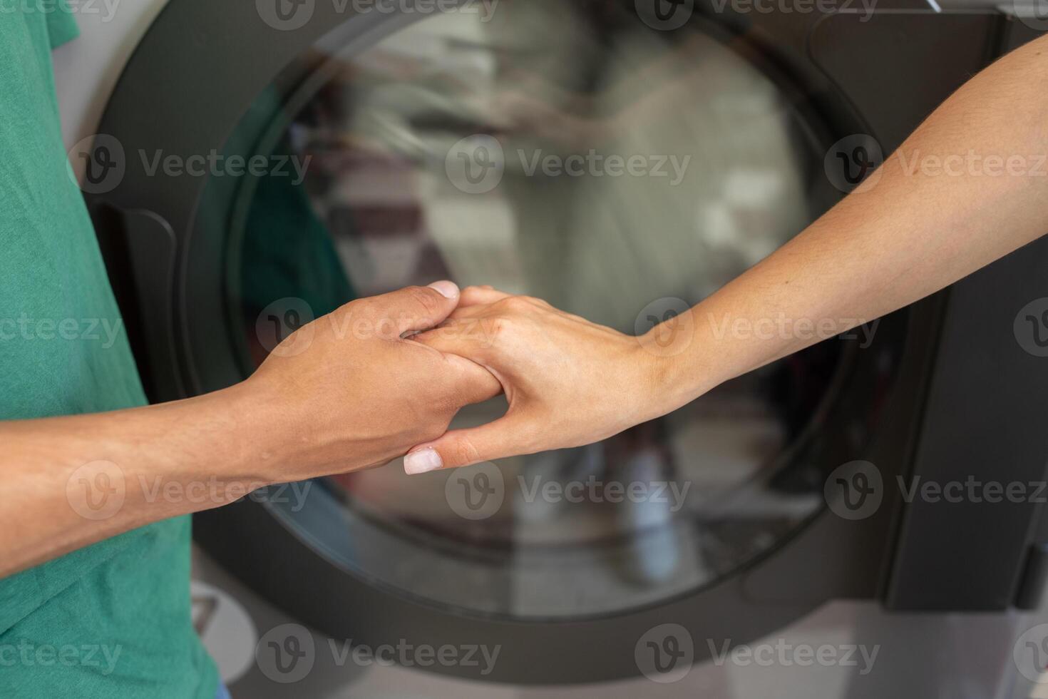 A couple is holding hands affectionately in a cozy laundry room, enjoying a moment together while a washing machine runs nearby. They appear relaxed and connected during this everyday activity. photo