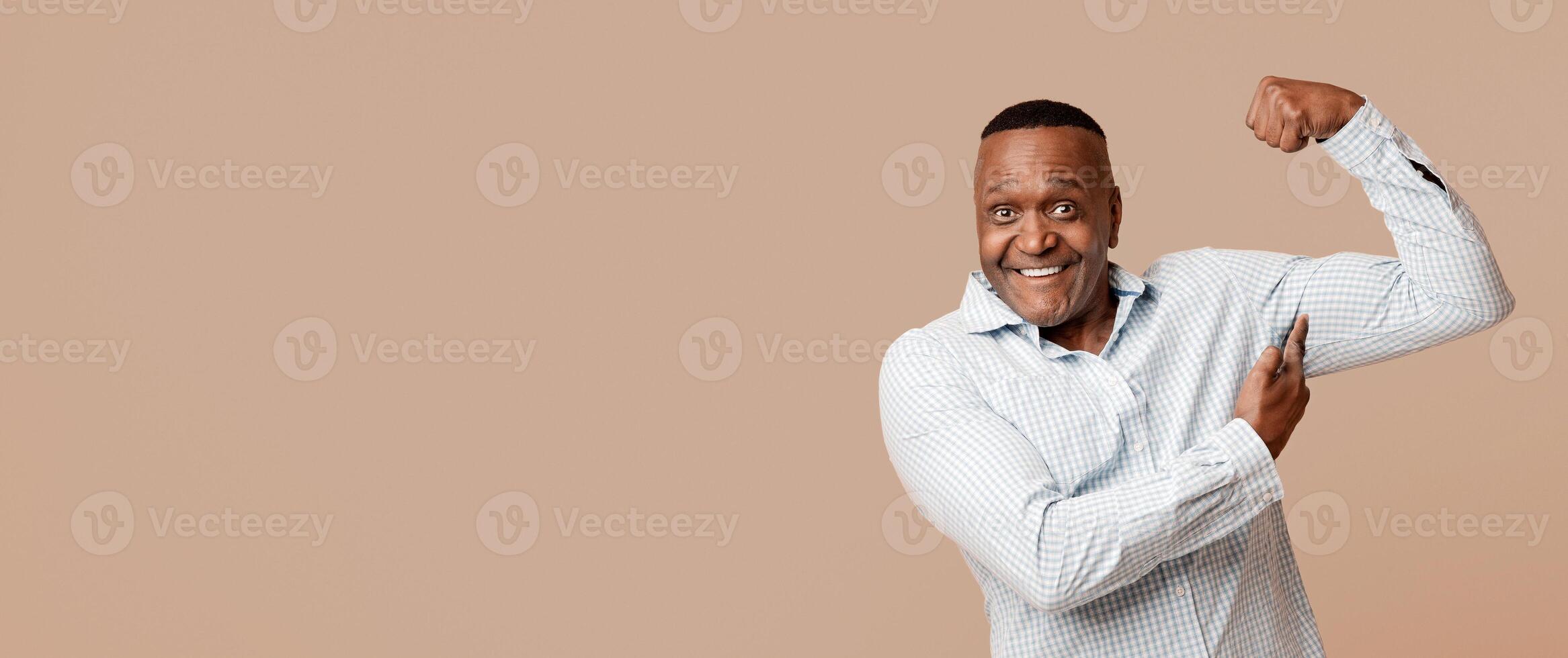 Still strong. Positive mature african american man showing his biceps, orange studio background photo
