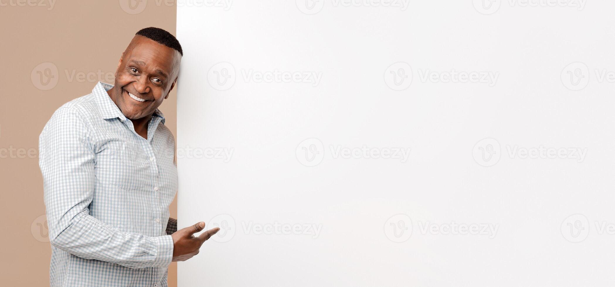 Look here. Positive mature man pointing at blank white placard, empty space photo