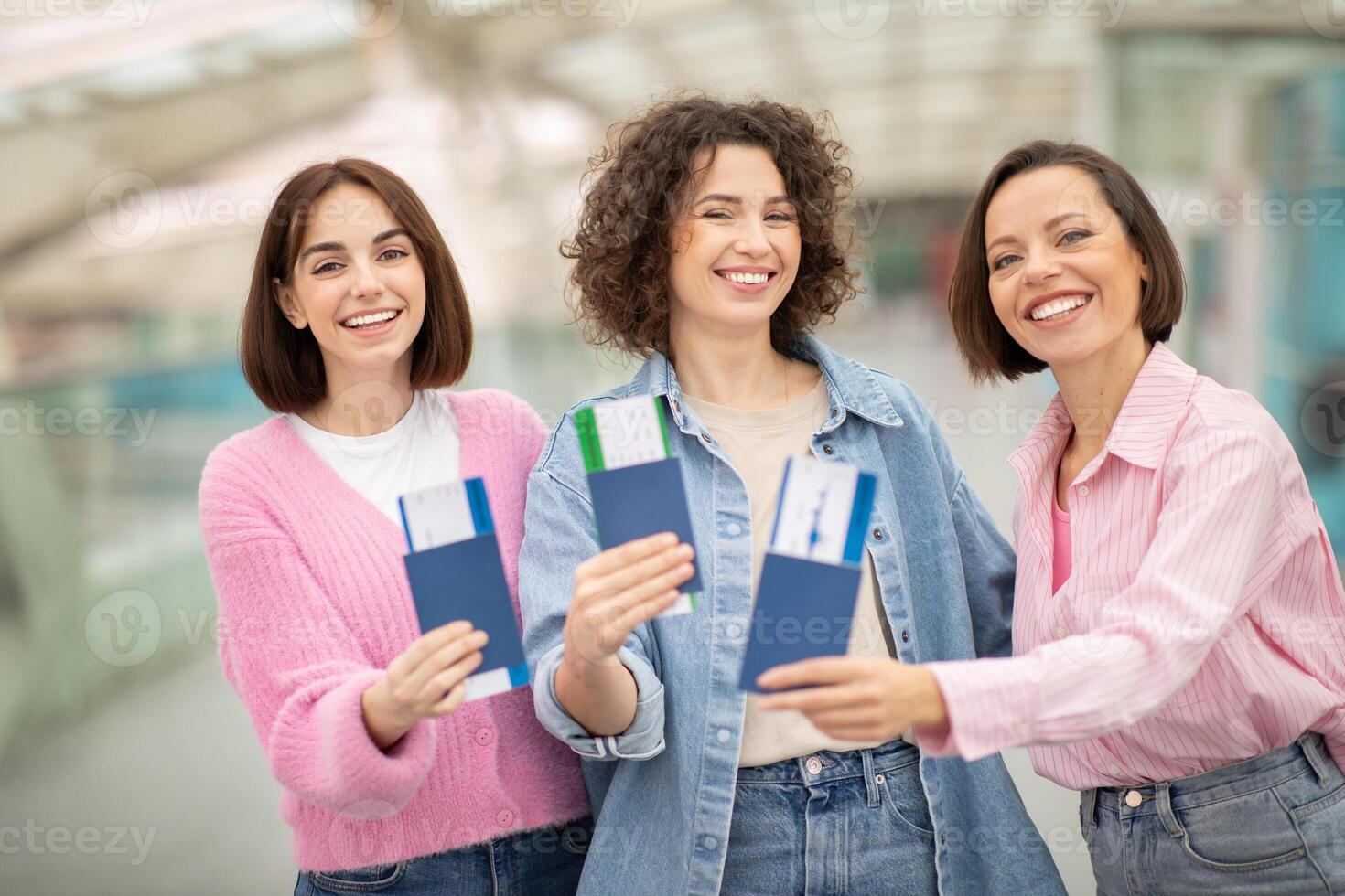 Three friends stand together at an airport terminal, excitedly displaying their passports. They share smiles and laughter, ready for their upcoming adventure together. photo