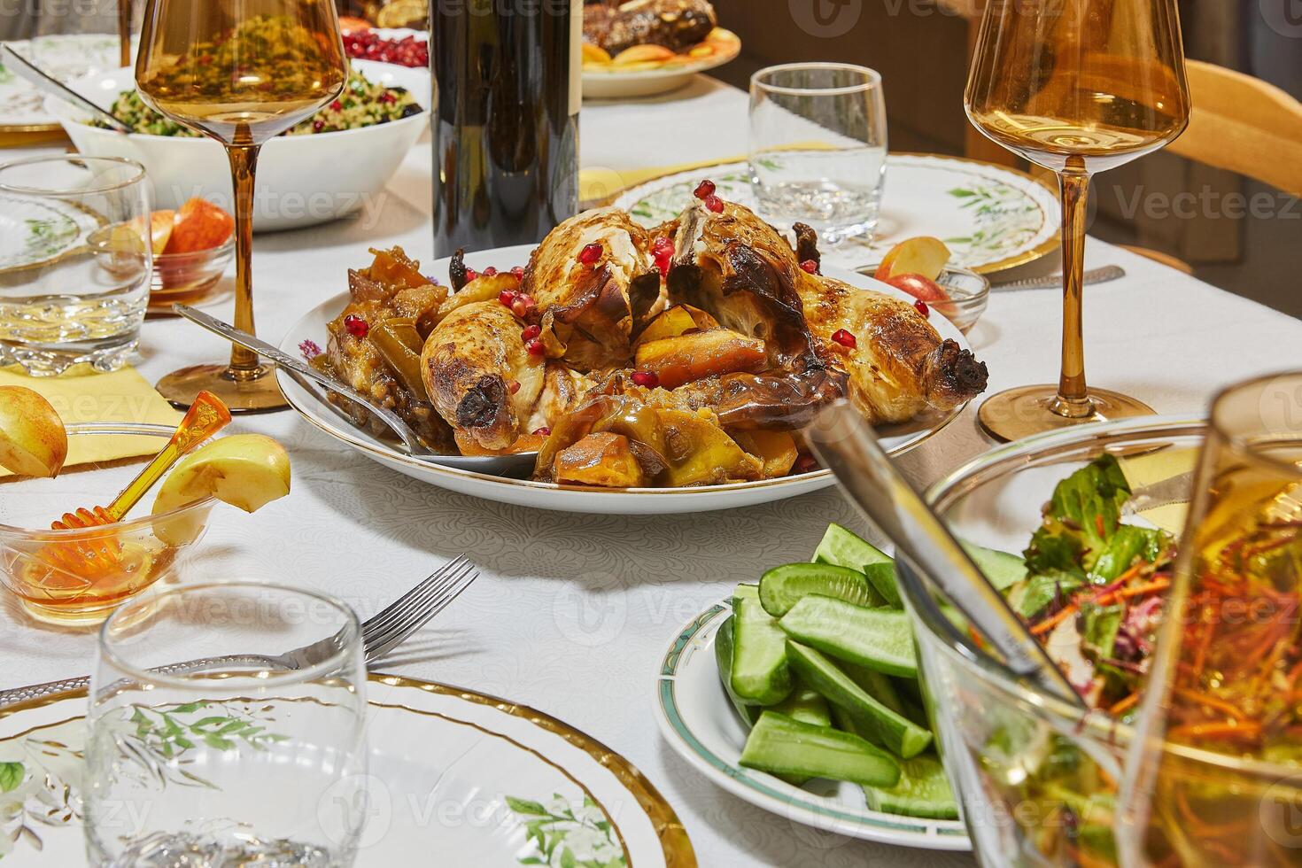 A golden roasted chicken garnished with pomegranate seeds, presented elegantly on a dining table with glasses and side dishes. photo