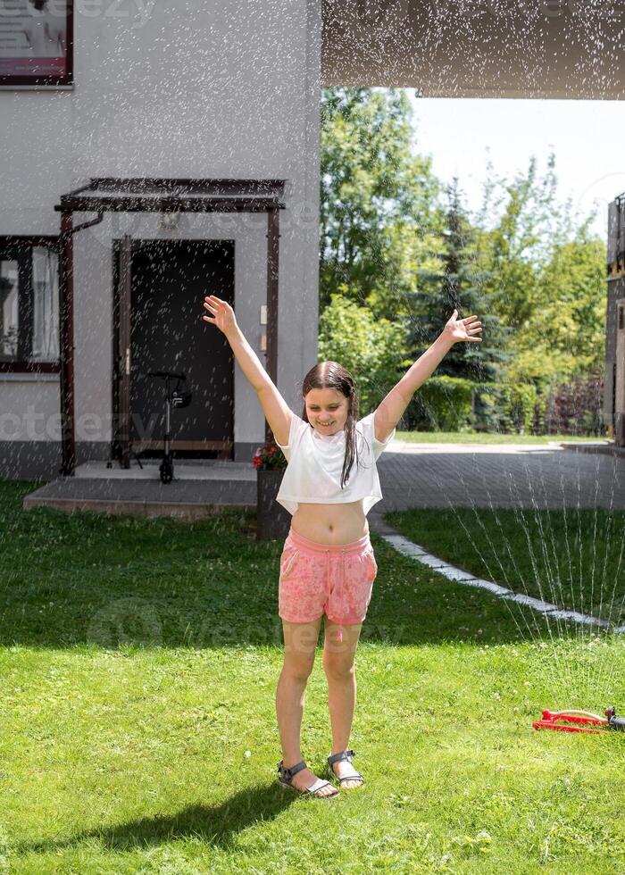 A girl jumps under a sprinkler on a hot summer day photo