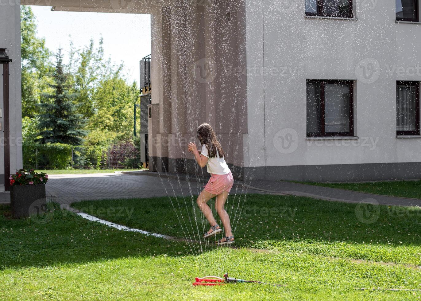 A girl jumps under a sprinkler on a hot summer day photo