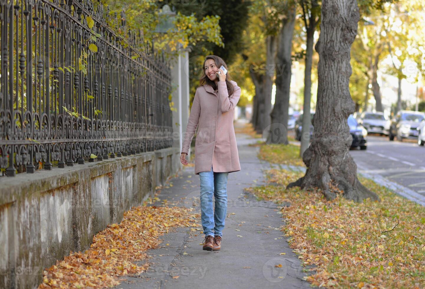 A woman talking on a phone at the street on a sunny autumn day. A woman smiles while using a mobile smartphone device photo
