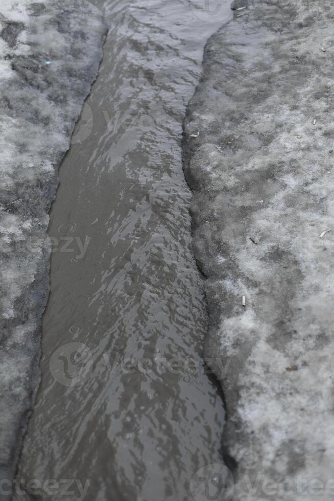 Dirty water flows on asphalt. Flow of water along road. Cloudy liquid. photo