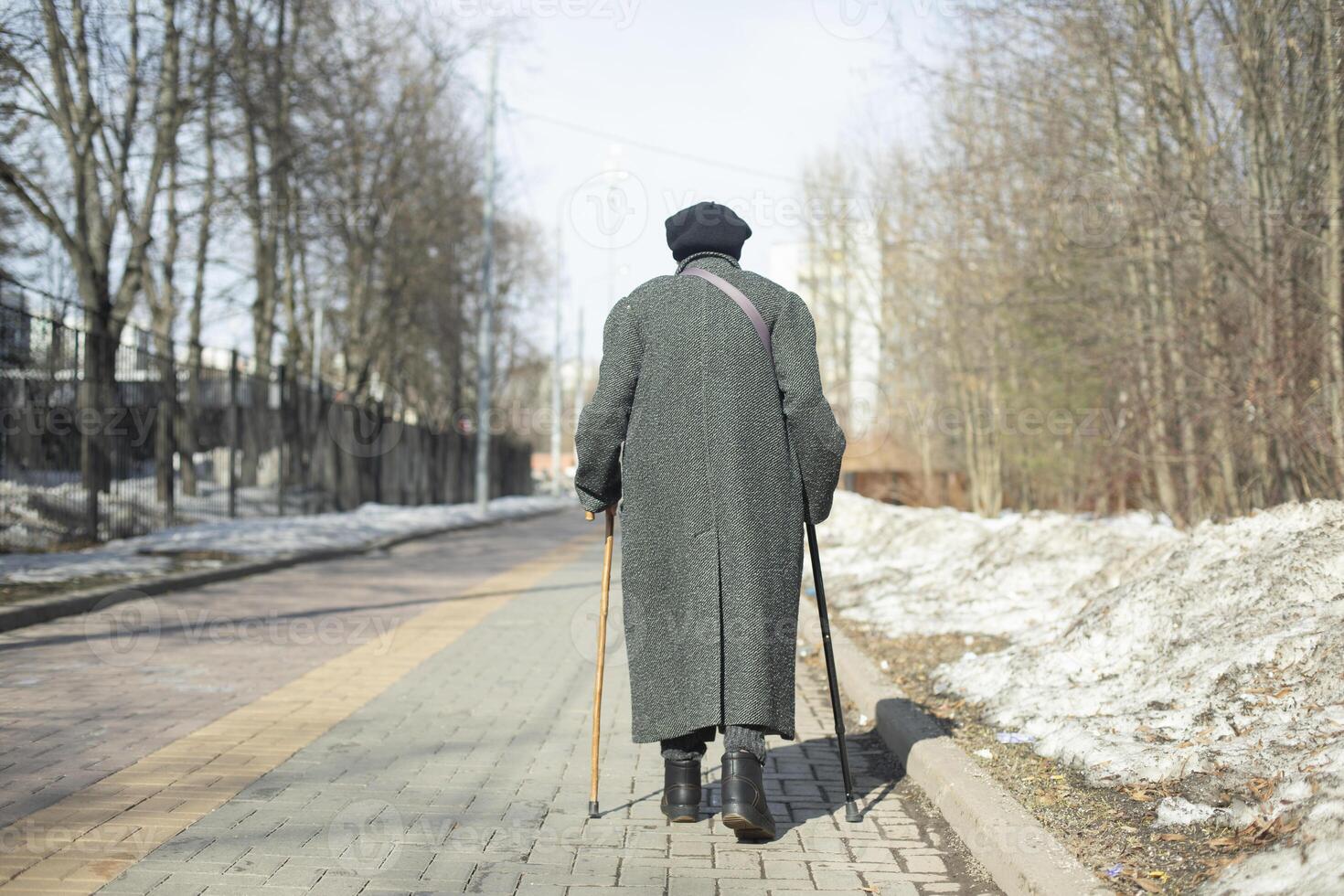 Pensioner walks down road. Old woman from back on street. One person walks through city. photo