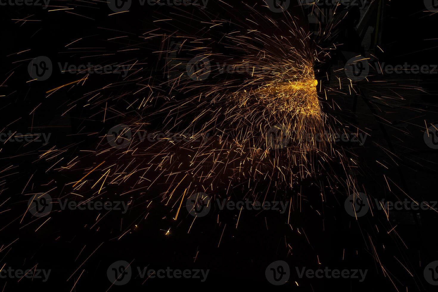 Sparks in dark. Lots of bright lights on black background. Burning metal particles fly in different directions. photo