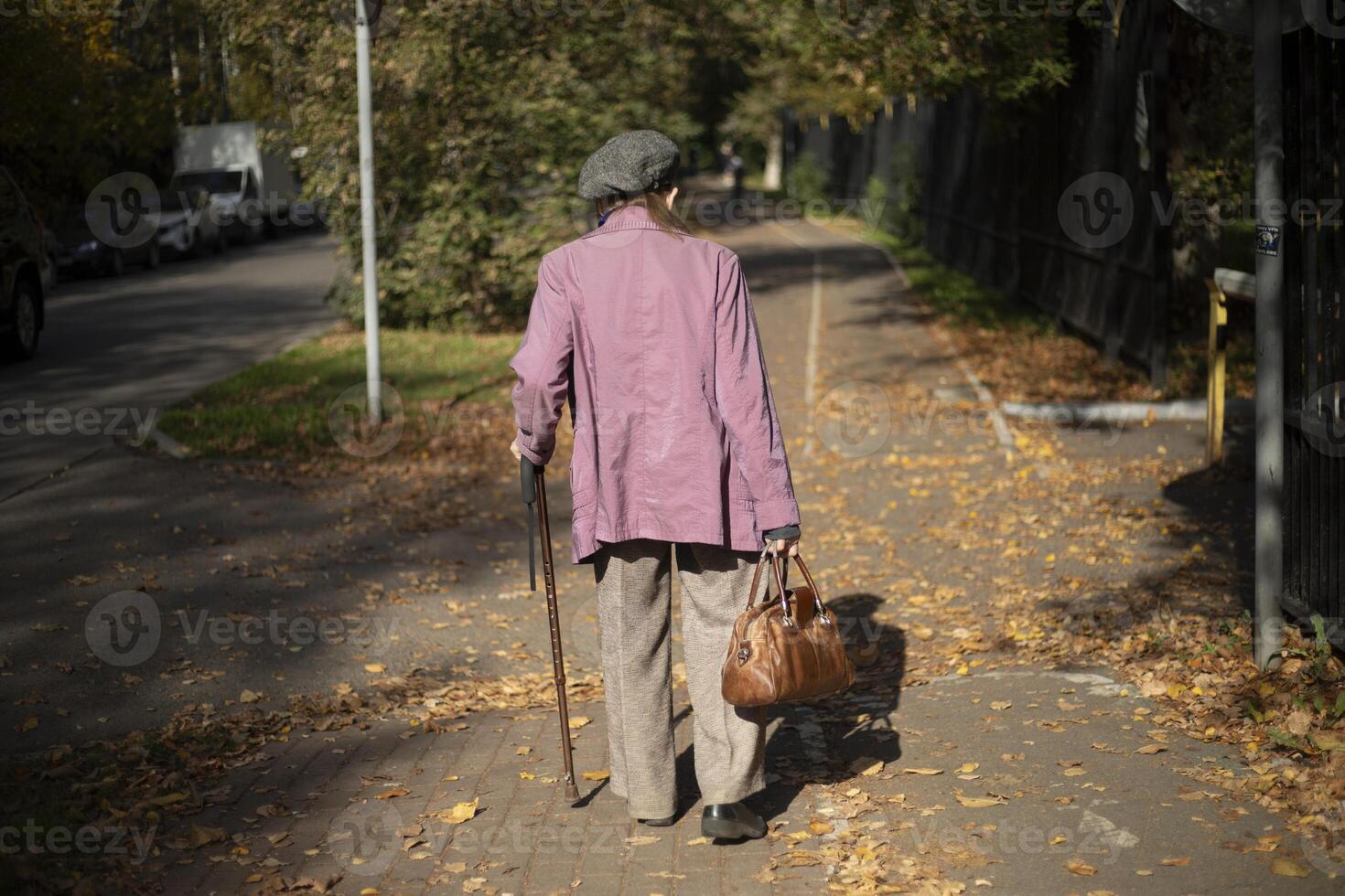 A pensioner walks down the street. An elderly man in town. Pole for support when walking. photo