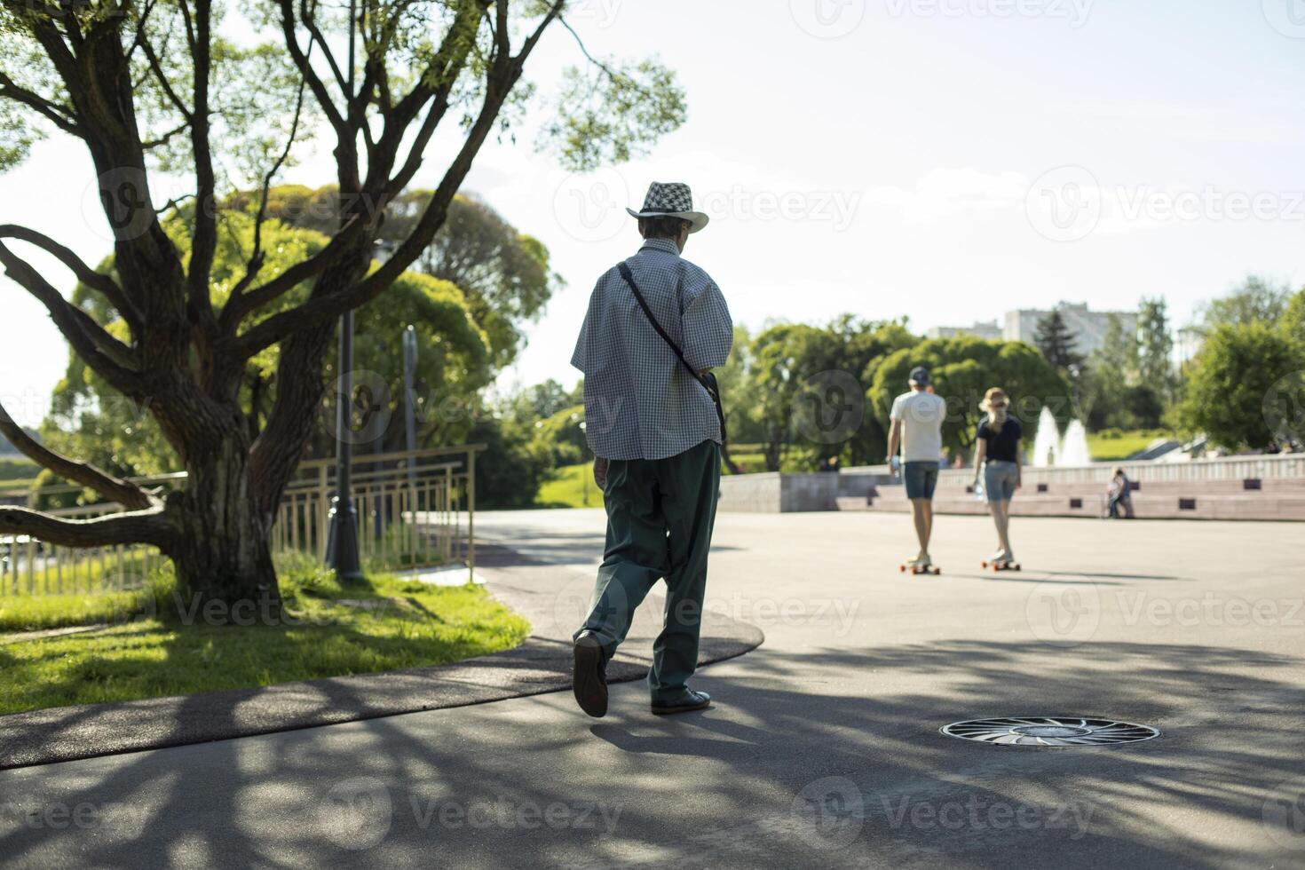 Guy walks through park in summer. Walking around city on summer day. Man from behind on street. photo