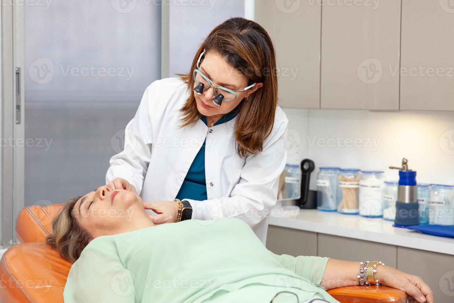 Dermatologist making a routine checkup on a senior famale patient using a binocular loupe. photo