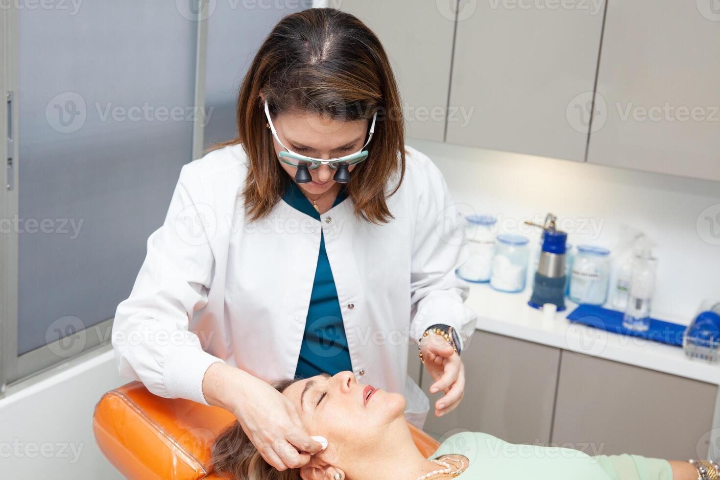 Dermatologist making a routine checkup on a senior famale patient using a binocular loupe. photo