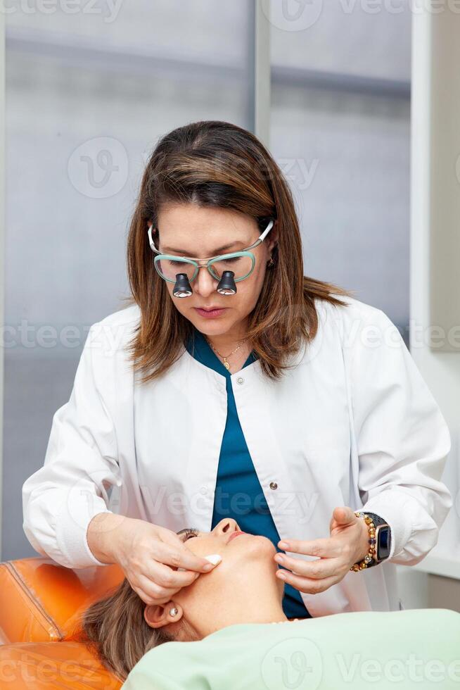 Dermatologist making a routine checkup on a senior famale patient using a binocular loupe. photo