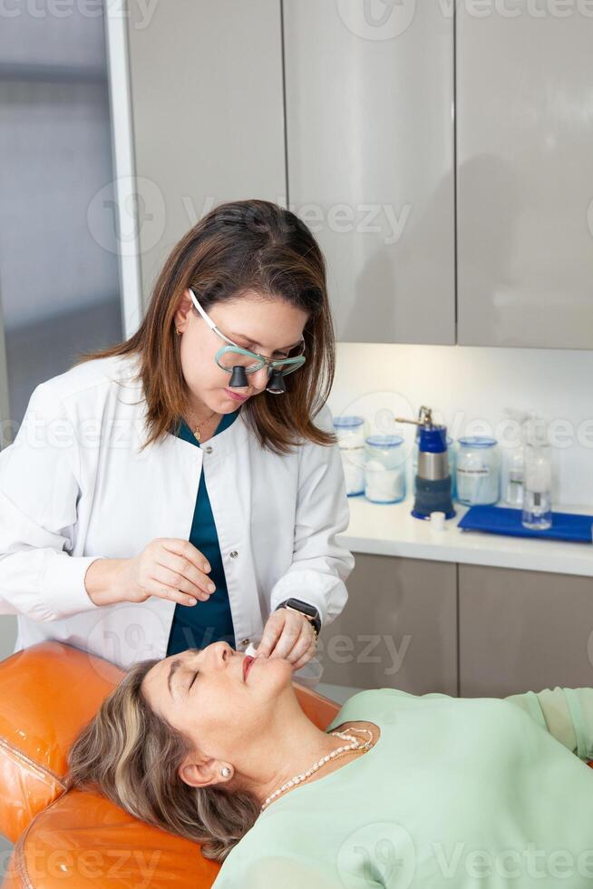 Dermatologist making a routine checkup on a senior famale patient using a binocular loupe. photo