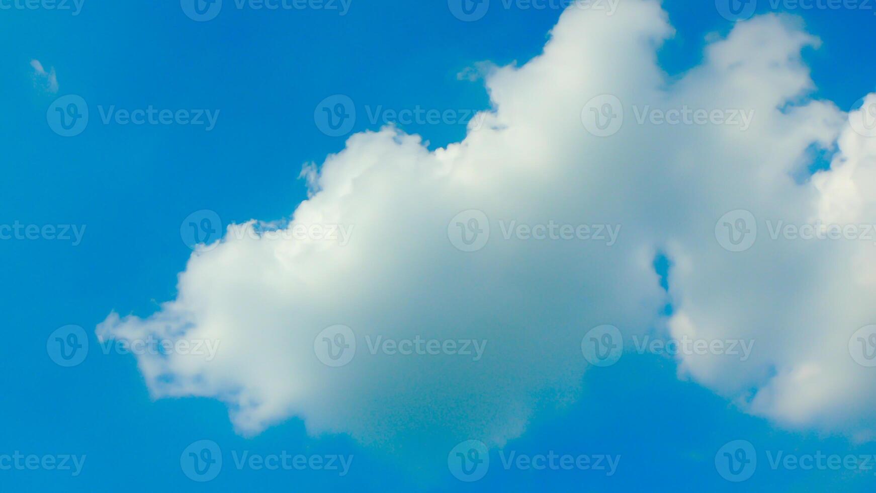 A single, fluffy white cloud drifts across a clear blue sky. The cloud is small and delicate, with soft, rounded edges. The sky is a deep, vibrant blue, with no other clouds in sight. photo
