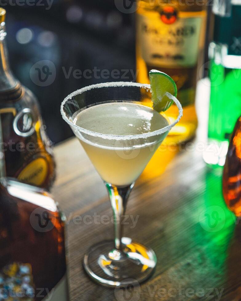 Cocktail glass standing on bar counter with bottles in background photo