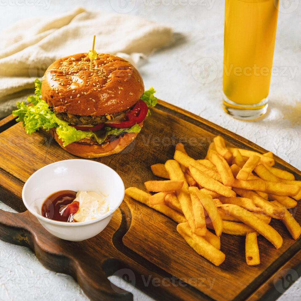 Delicious burger served on wooden board with french fries and dipping sauce photo