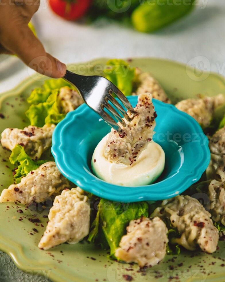 Person picking up manti dumpling with fork from plate photo
