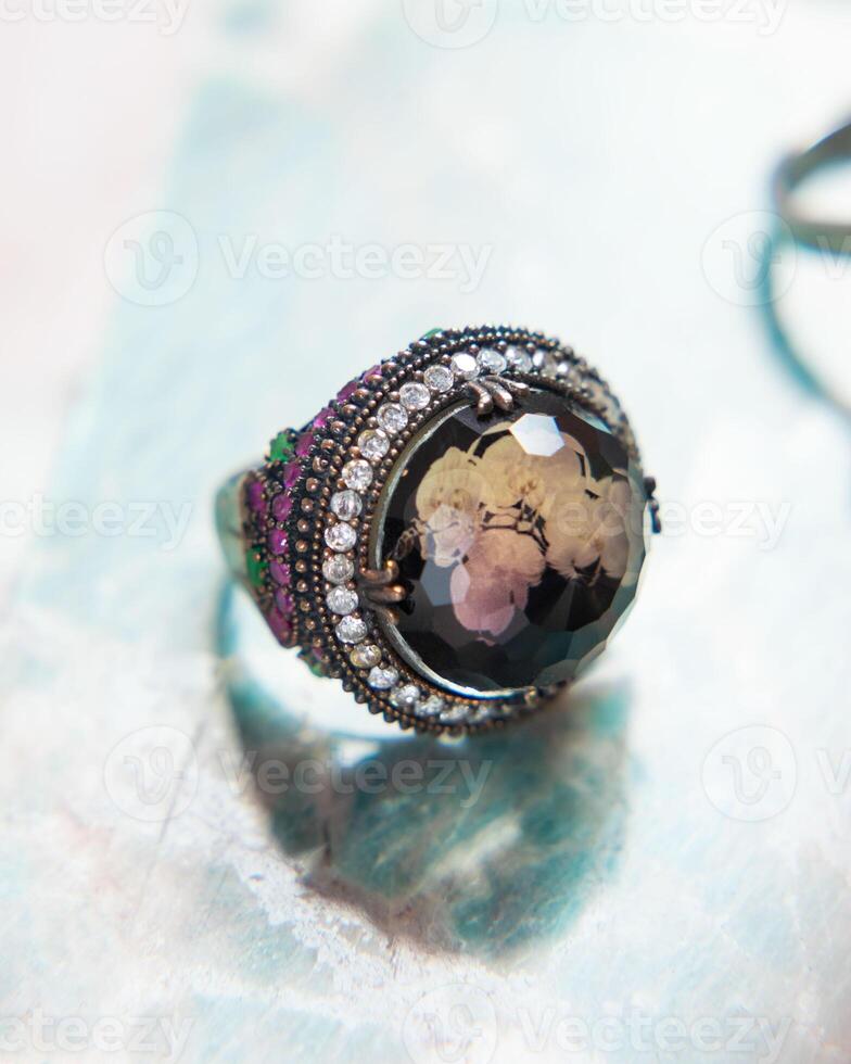 Silver ring with large stone and small emerald and ruby gemstones is lying on the table photo