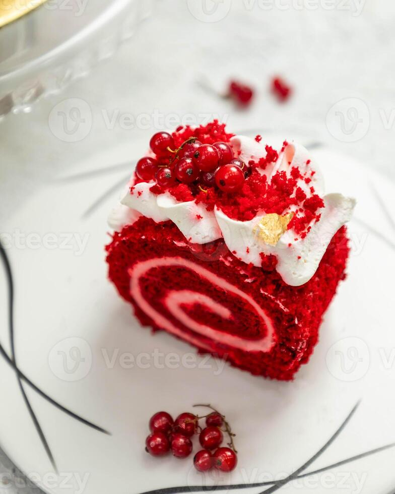 Red velvet swiss roll cake lying on white plate decorated with redcurrant and cream photo