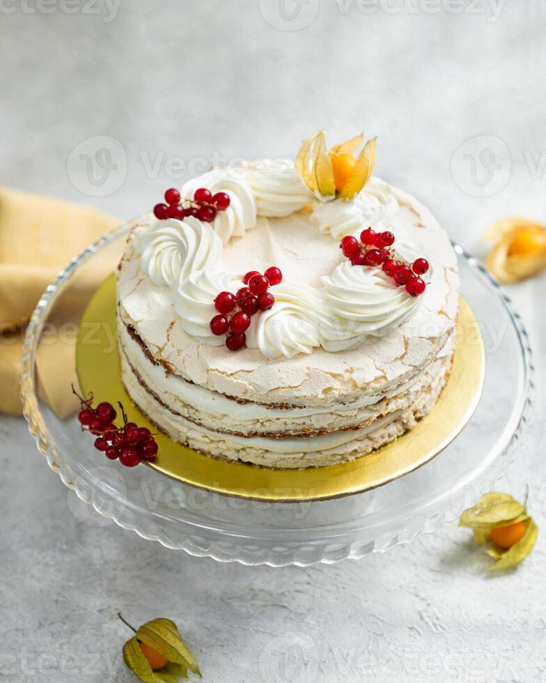 Delicious meringue cake decorated with redcurrant and cream cheese on glass stand photo