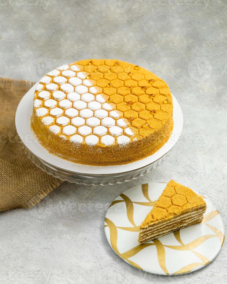 Honey cake decorated with honeycomb pattern standing on concrete background photo