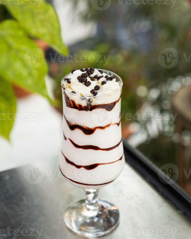 Delicious milkshake with chocolate syrup and whipped cream standing on table photo