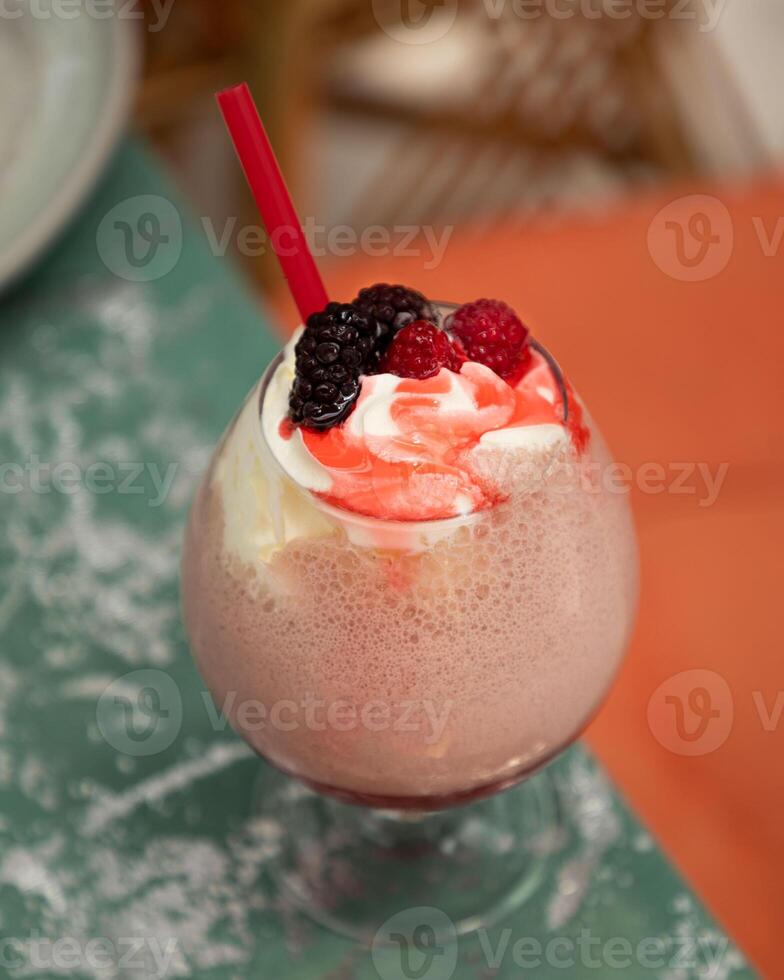 Delicious pink cocktail topped with whipped cream, berries, and red straw is sitting on a table photo