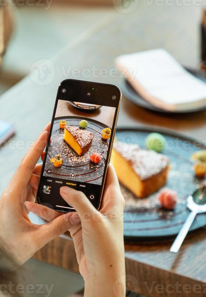 Woman taking photo of cake using smartphone in restaurant
