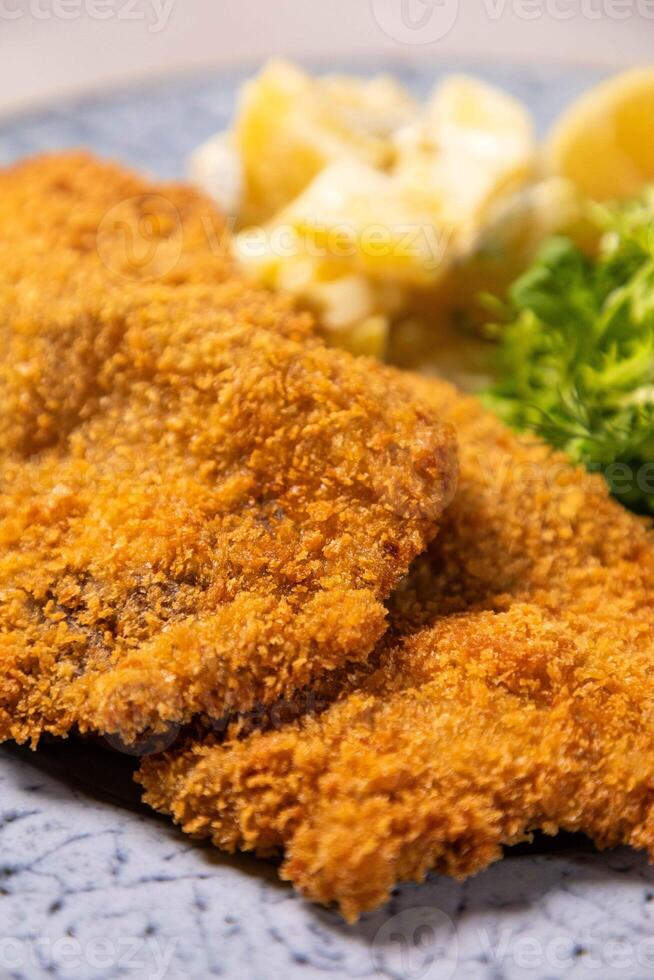 Breaded chicken schnitzel is served on plate with potatoes salad and garnish photo
