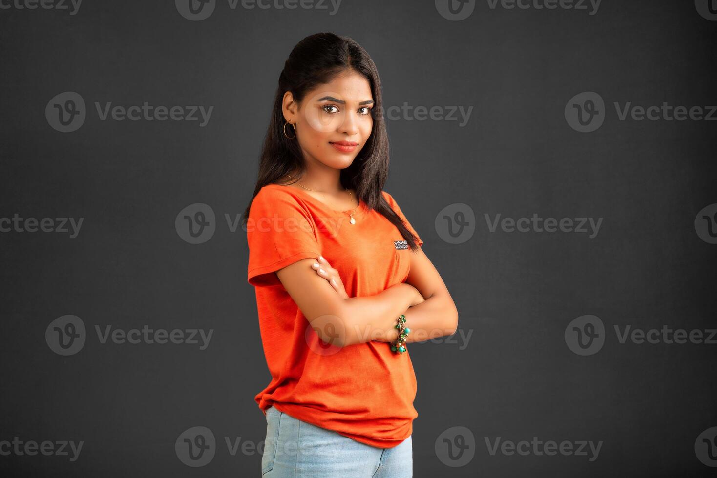 Portrait of a beautiful, smiling, young girl posing with hands-folded on gray background. photo