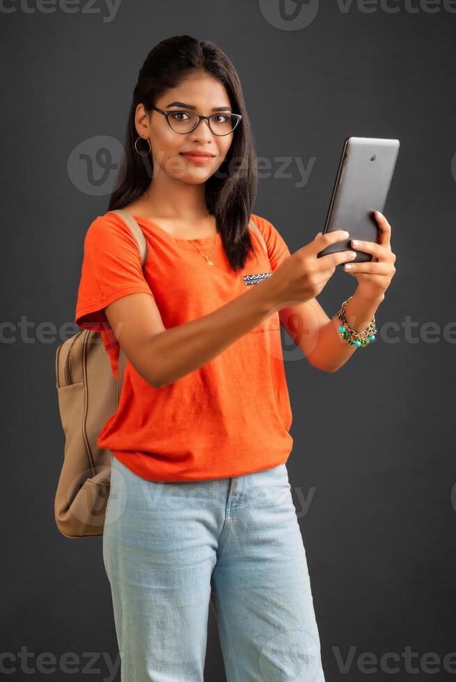 Beautiful young girl with a backpack using mobile phone or smartphone on gray background photo