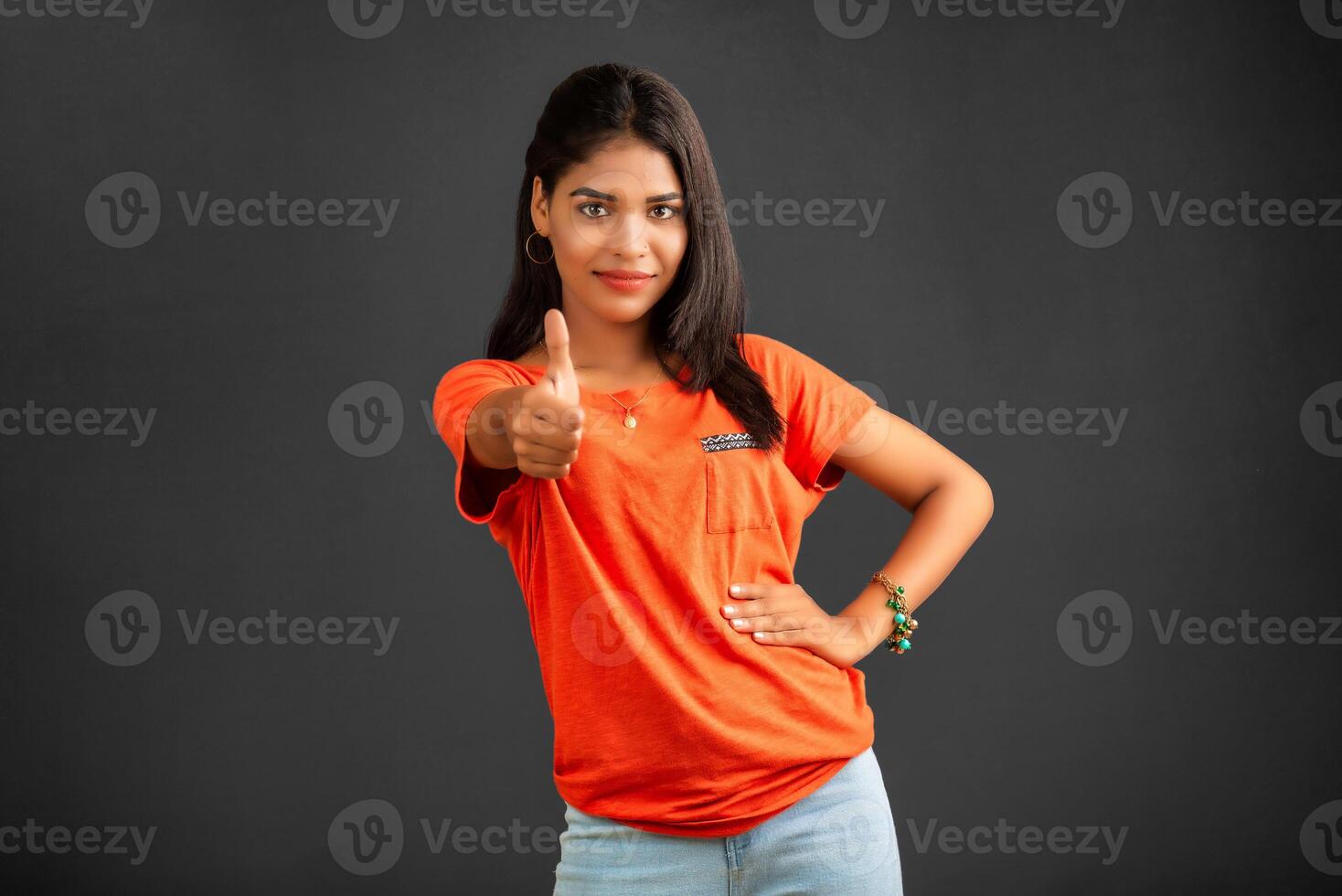 Young smiling girl showing ok sign or thumbs up on a grey background photo