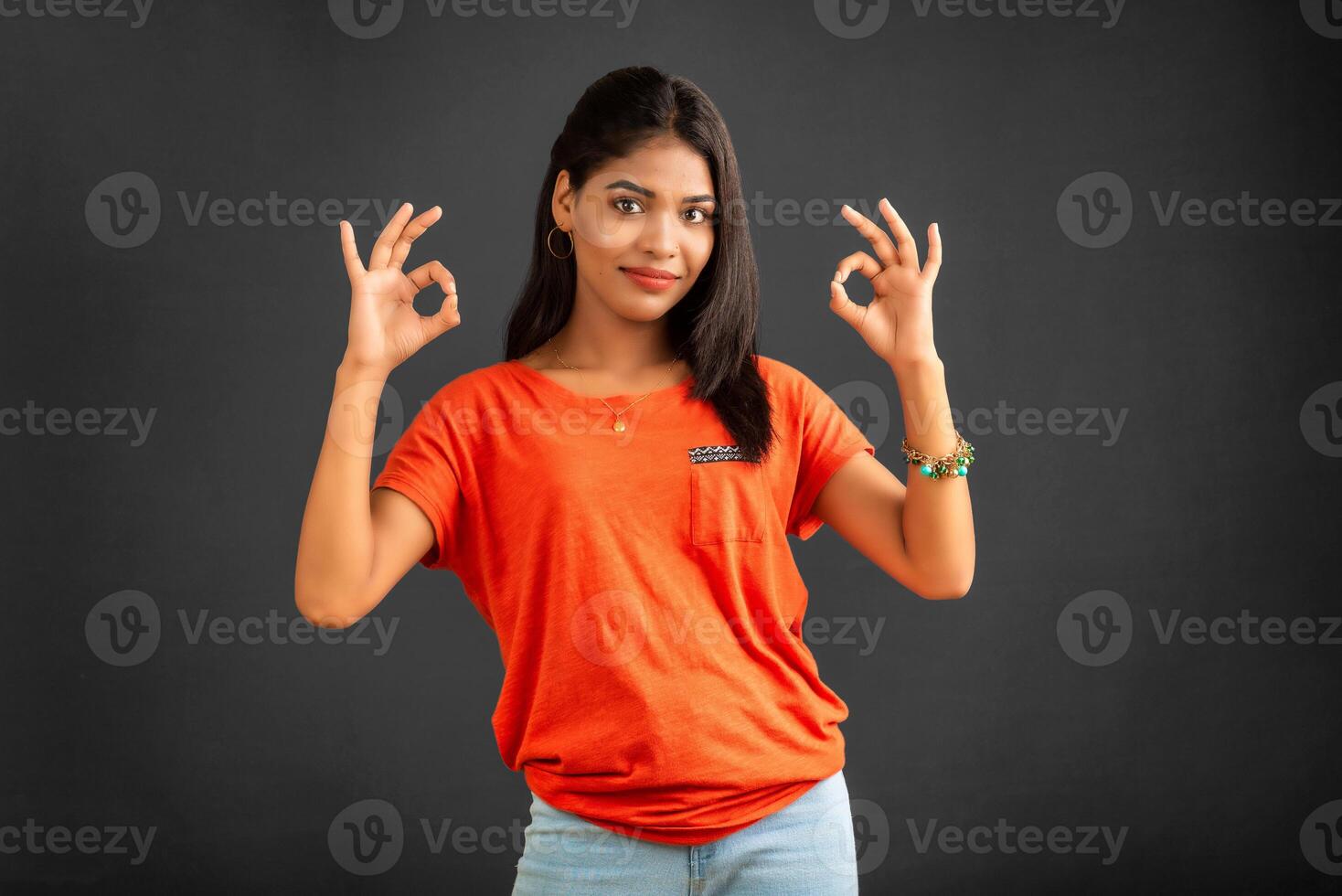 Young smiling girl showing ok sign or thumbs up on a grey background photo