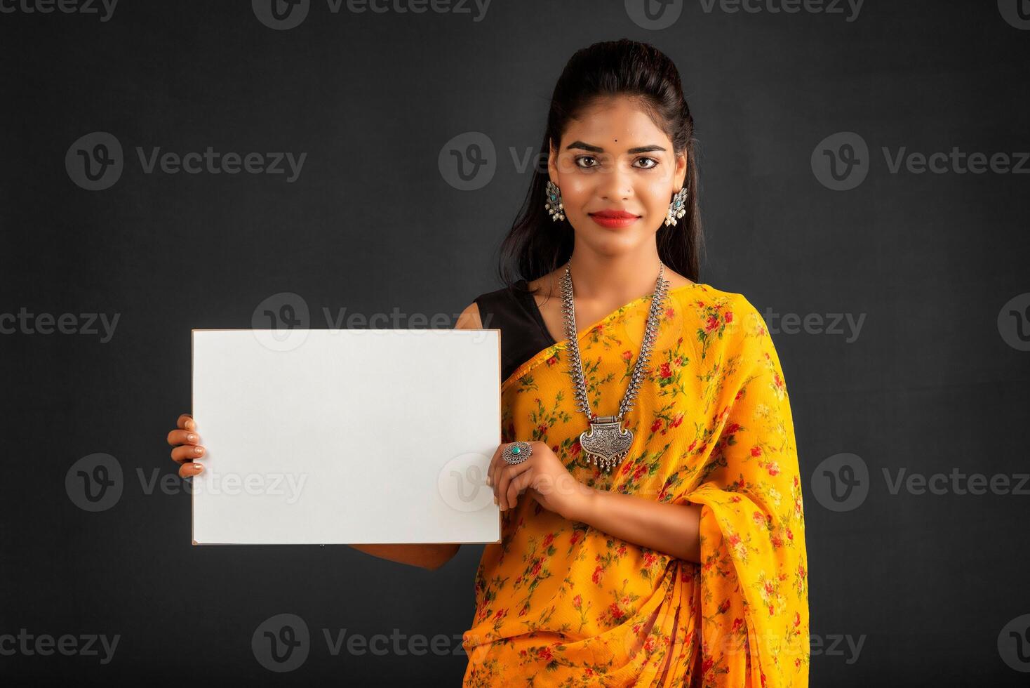 A young girl or businesswoman wearing a saree and holding a signboard in her hands on a gray background. photo