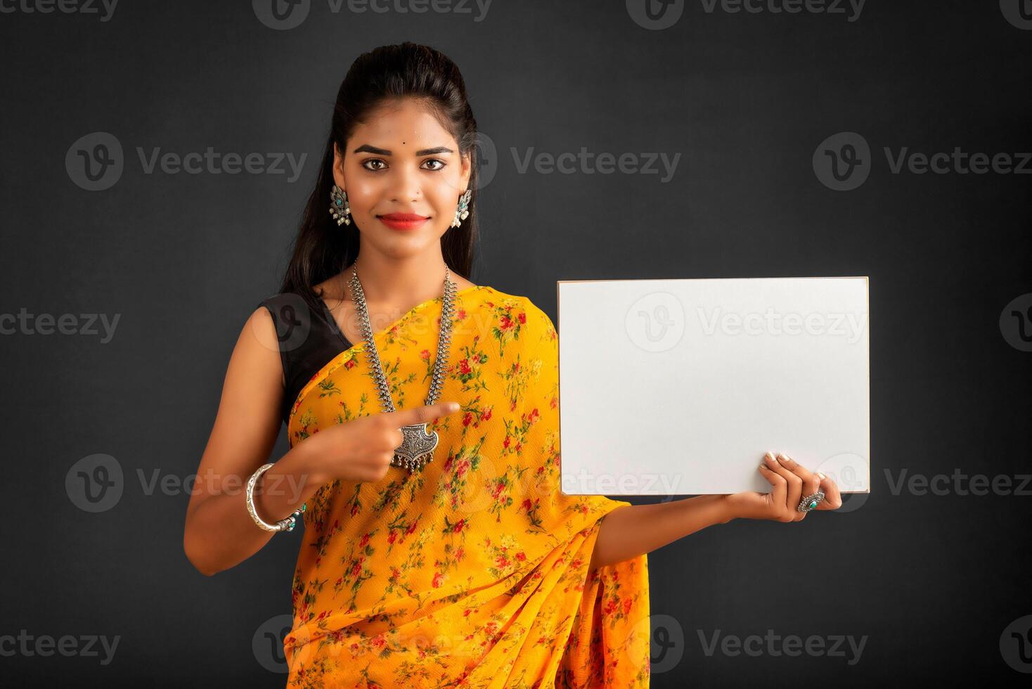 A young girl or businesswoman wearing a saree and holding a signboard in her hands on a gray background. photo
