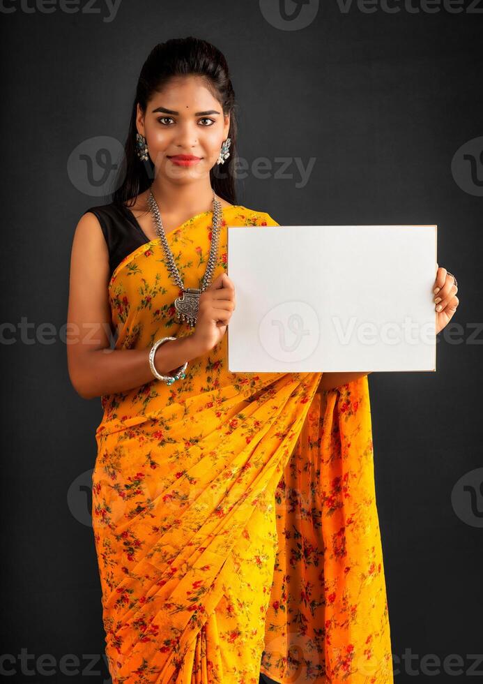 A young girl or businesswoman wearing a saree and holding a signboard in her hands on a gray background. photo