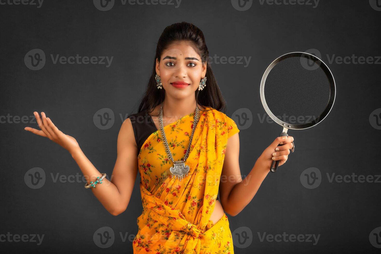 Young girl holding and posing with kitchen utensils pan on a grey background photo