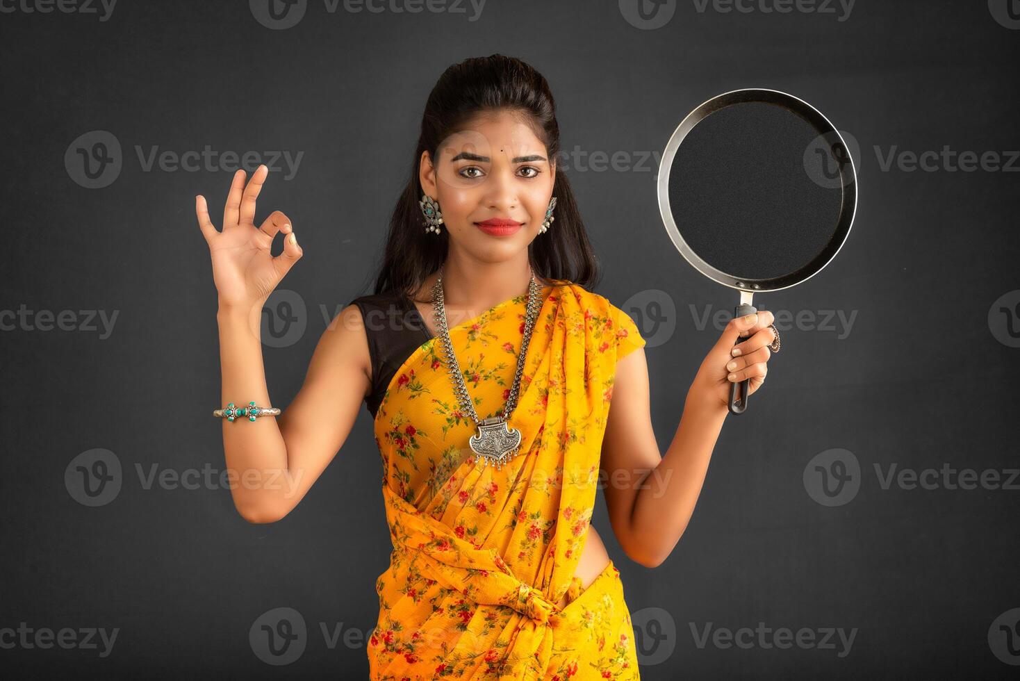 Young girl holding and posing with kitchen utensils pan on a grey background photo