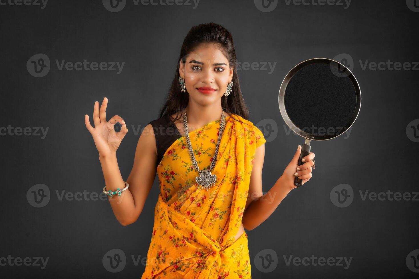 Young girl holding and posing with kitchen utensils pan on a grey background photo