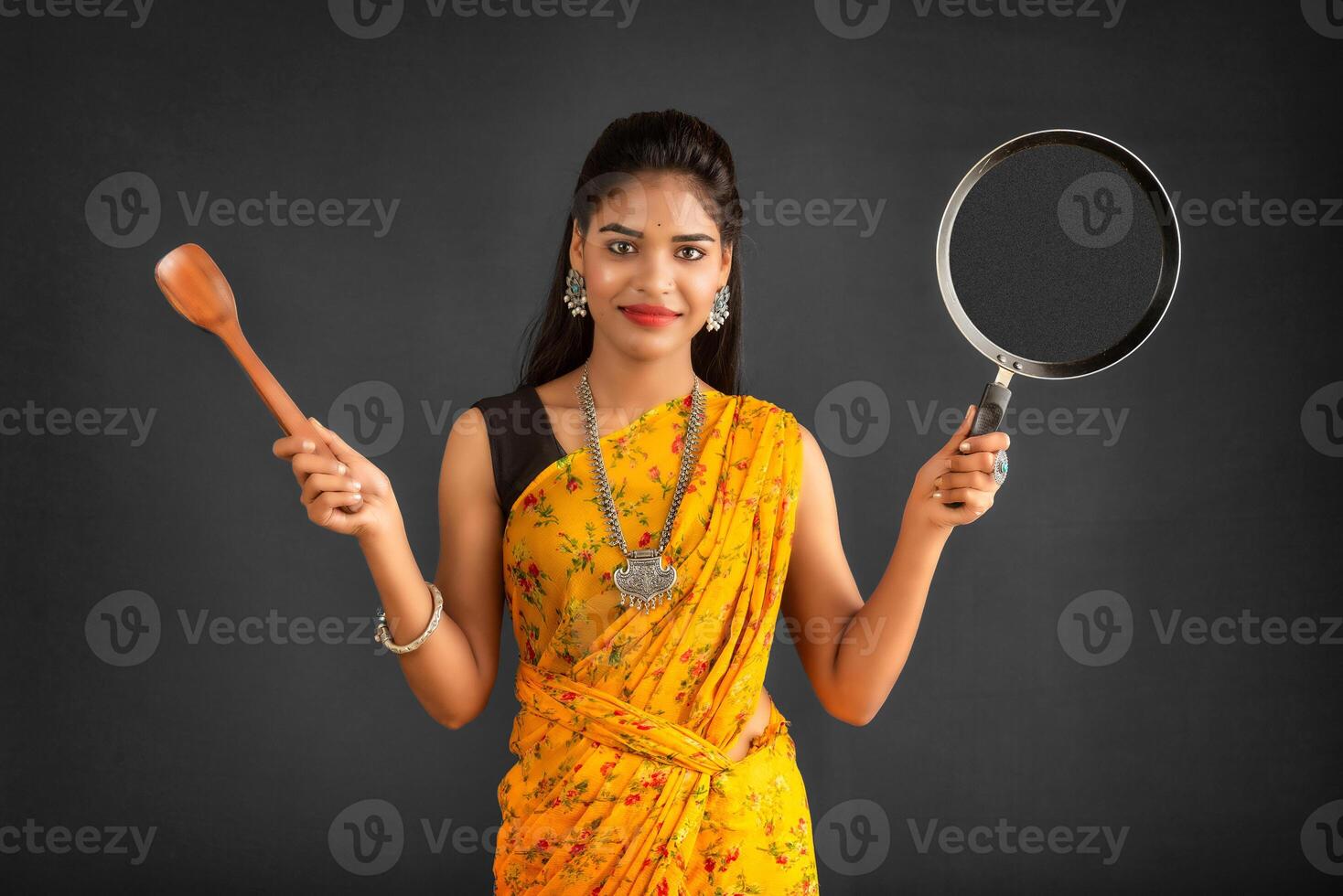 Young girl holding and posing with kitchen utensils pan on a grey background photo
